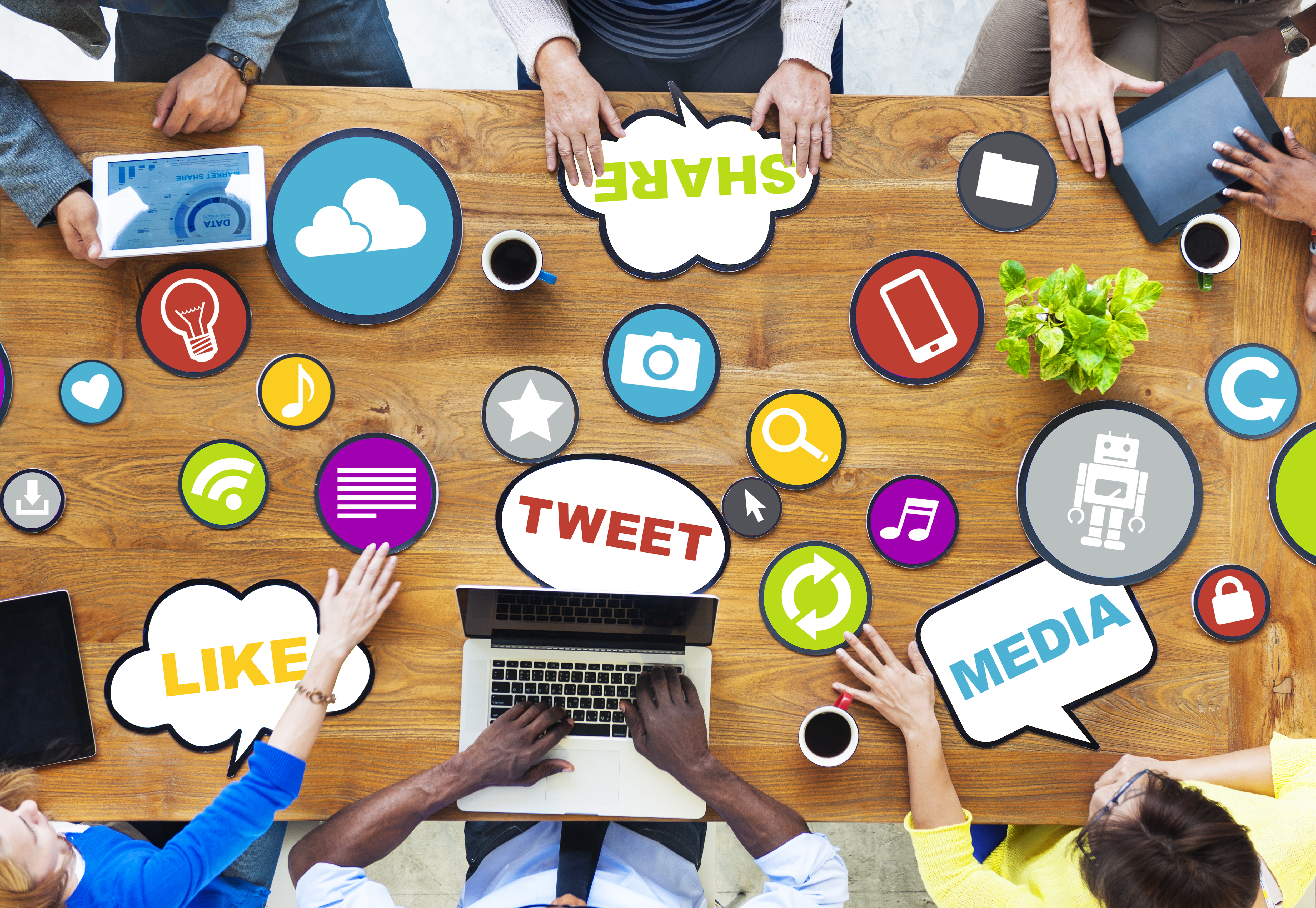 Six people sitting at a wooden table that contains signs of different shapes and colors pertaining to social media